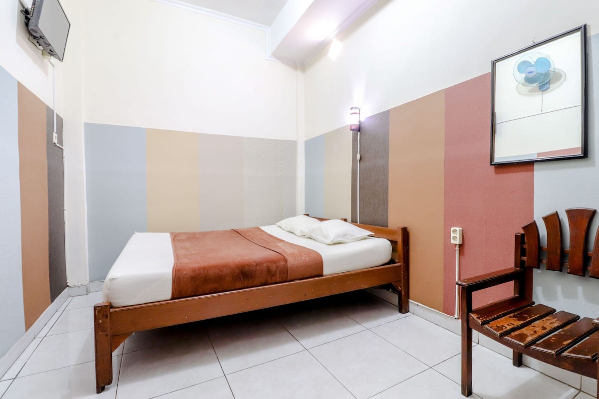 A single bed with a brown headboard, a bedside table, and a wall-mounted fan.