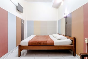 Una cama bien hecha con una manta marrón y almohadas blancas en una habitación con suelo de baldosas y paredes de colores pastel.
