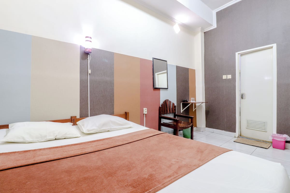 A hotel room with a bed, a chair, a desk, and a door.
