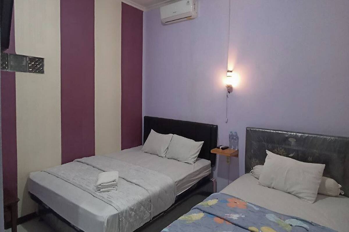 A room with two beds, a wall-mounted air conditioner, and a bedside table with a water bottle.