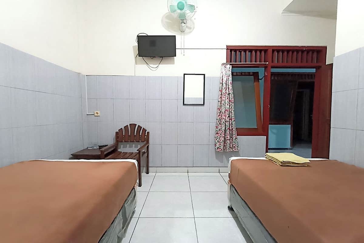 A small, clean room with two beds, a desk, a chair, a TV, and a window with a curtain.