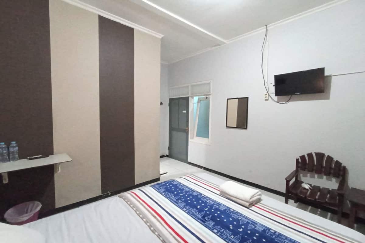 A hotel room with a bed, a TV mounted on the wall, a chair, and a small table.