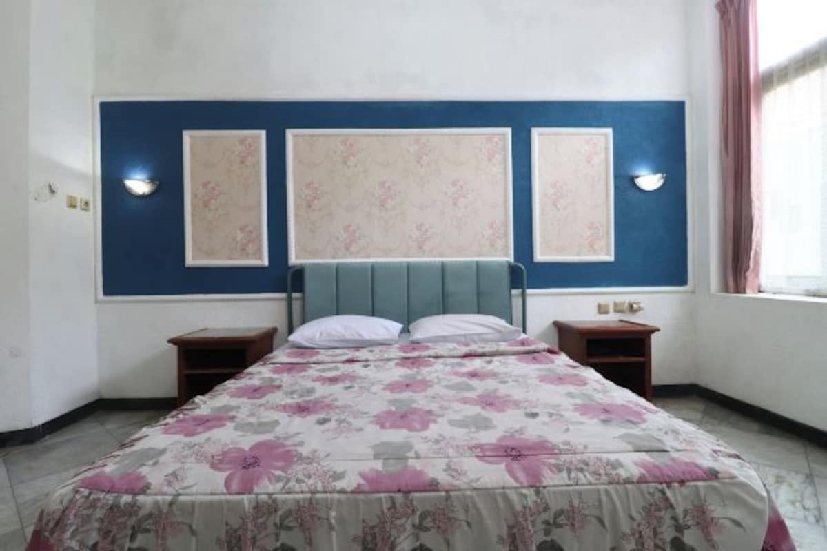 A bedroom with a bed, two bedside tables, and a headboard with wall-mounted lights.