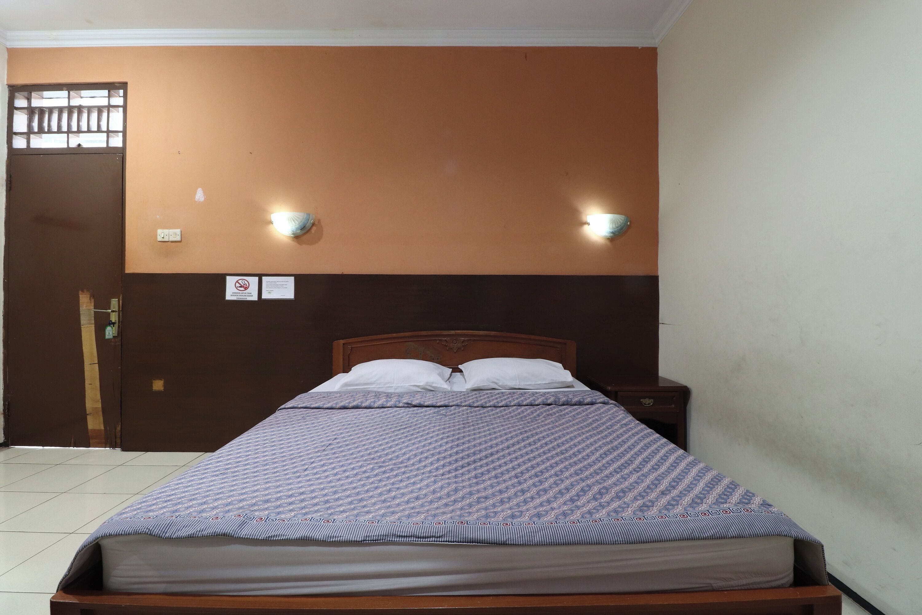 A single bed with a patterned bedspread, a wooden headboard, and two wall-mounted light fixtures.