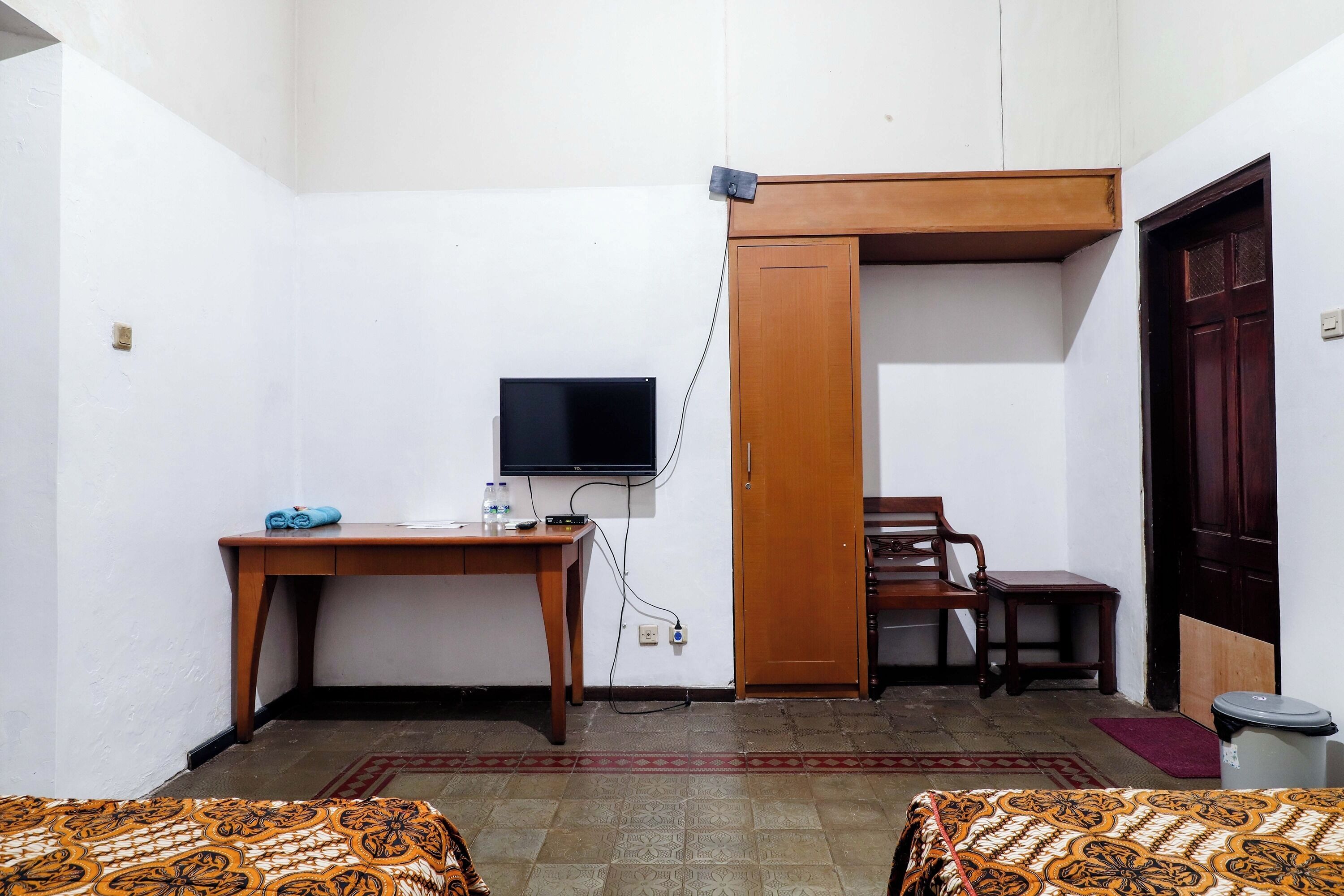 A small room with a bed, a desk with a computer, a television, and a door.