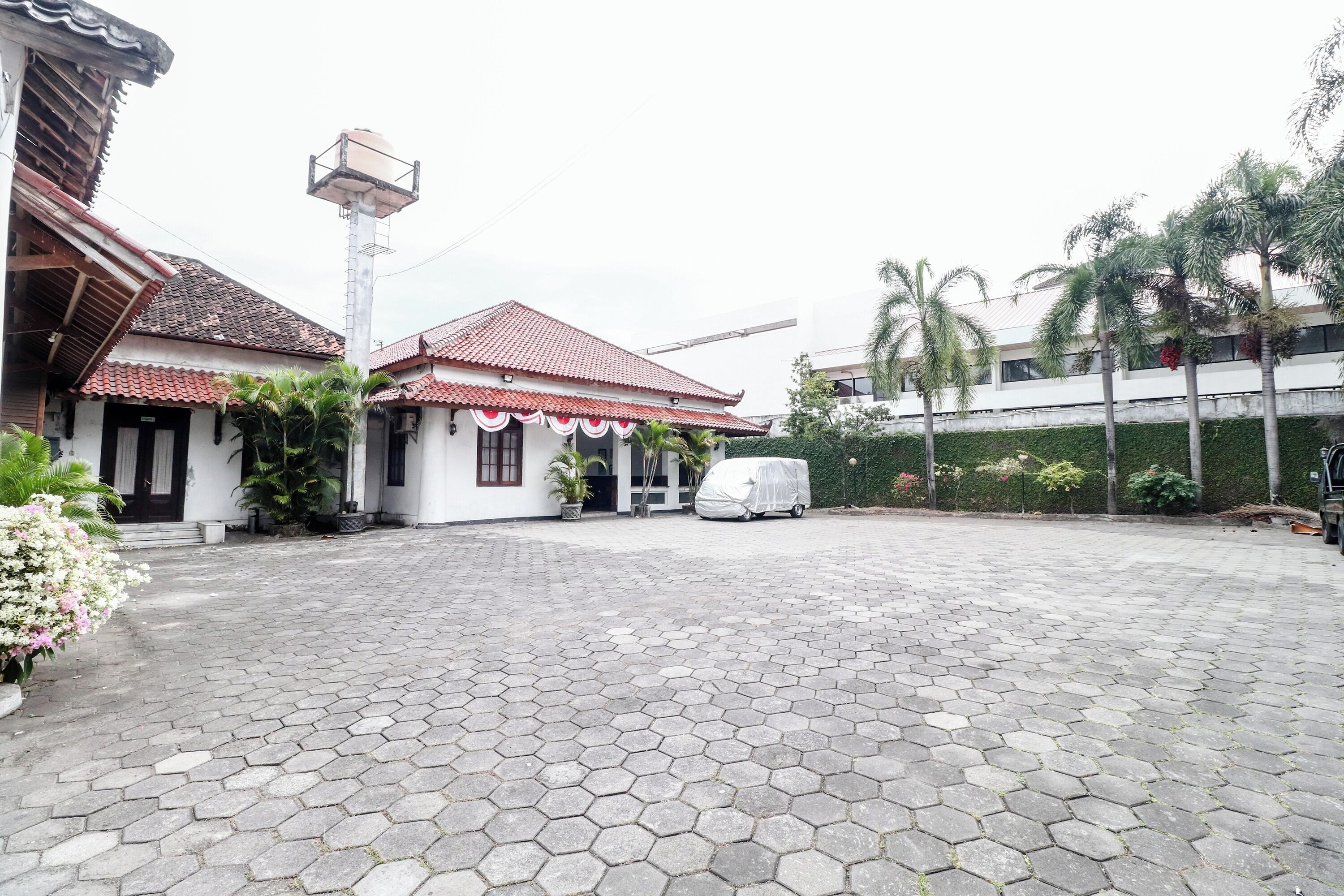 A courtyard with hexagonal paving, a covered vehicle, and a building with a red-tiled roof.