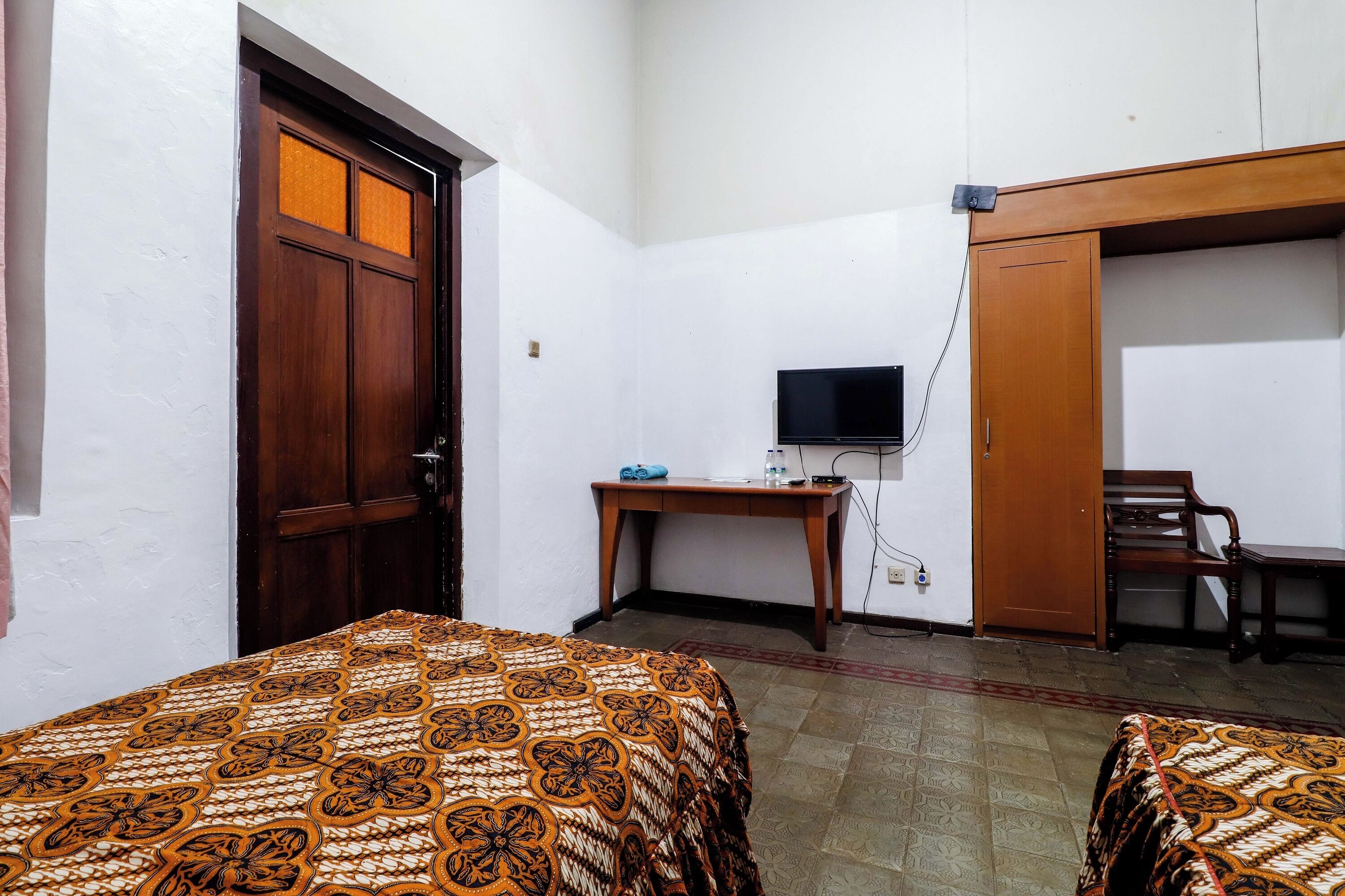 A room with two beds, a desk with a TV, a chair, and a wardrobe.