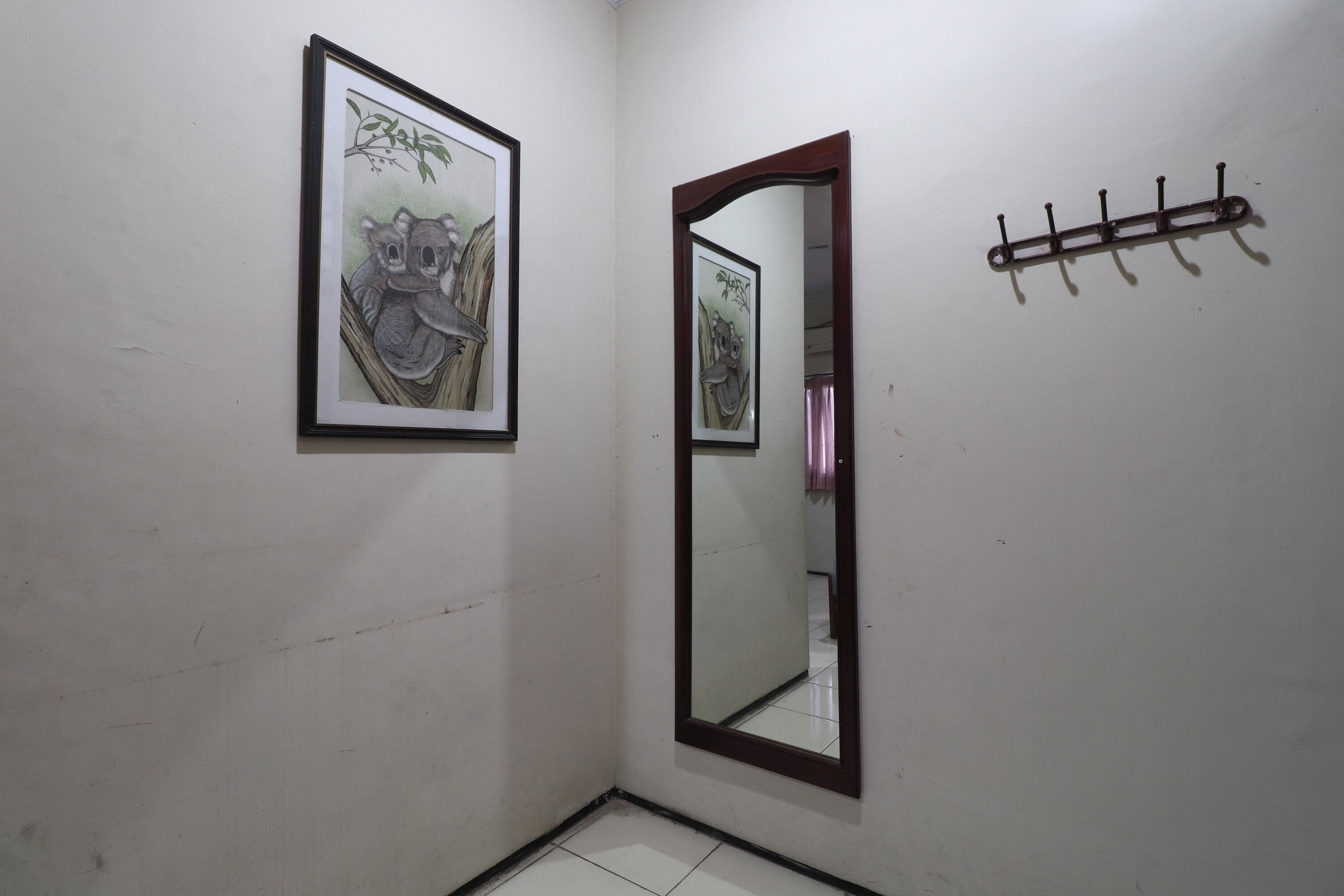 A hallway with a framed picture of a koala, a mirror, and a coat rack.