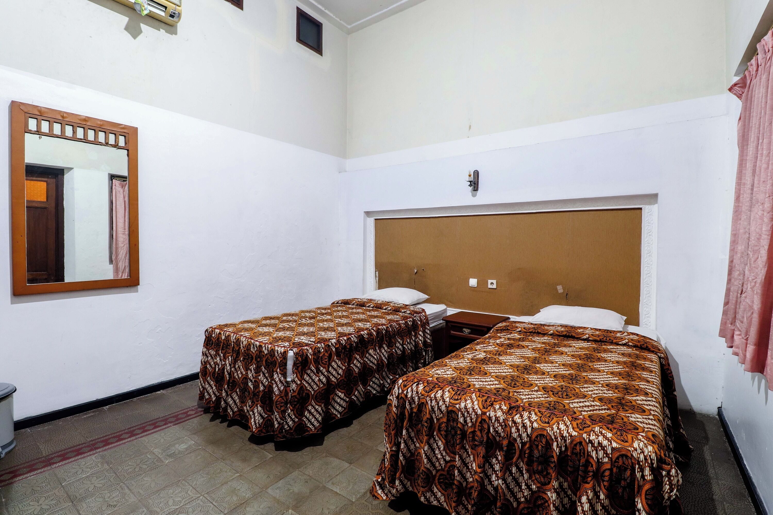 Ein Zimmer mit zwei Einzelbetten, einem hölzernen Kopfteil, einem Spiegel und einem kleinen Tisch.