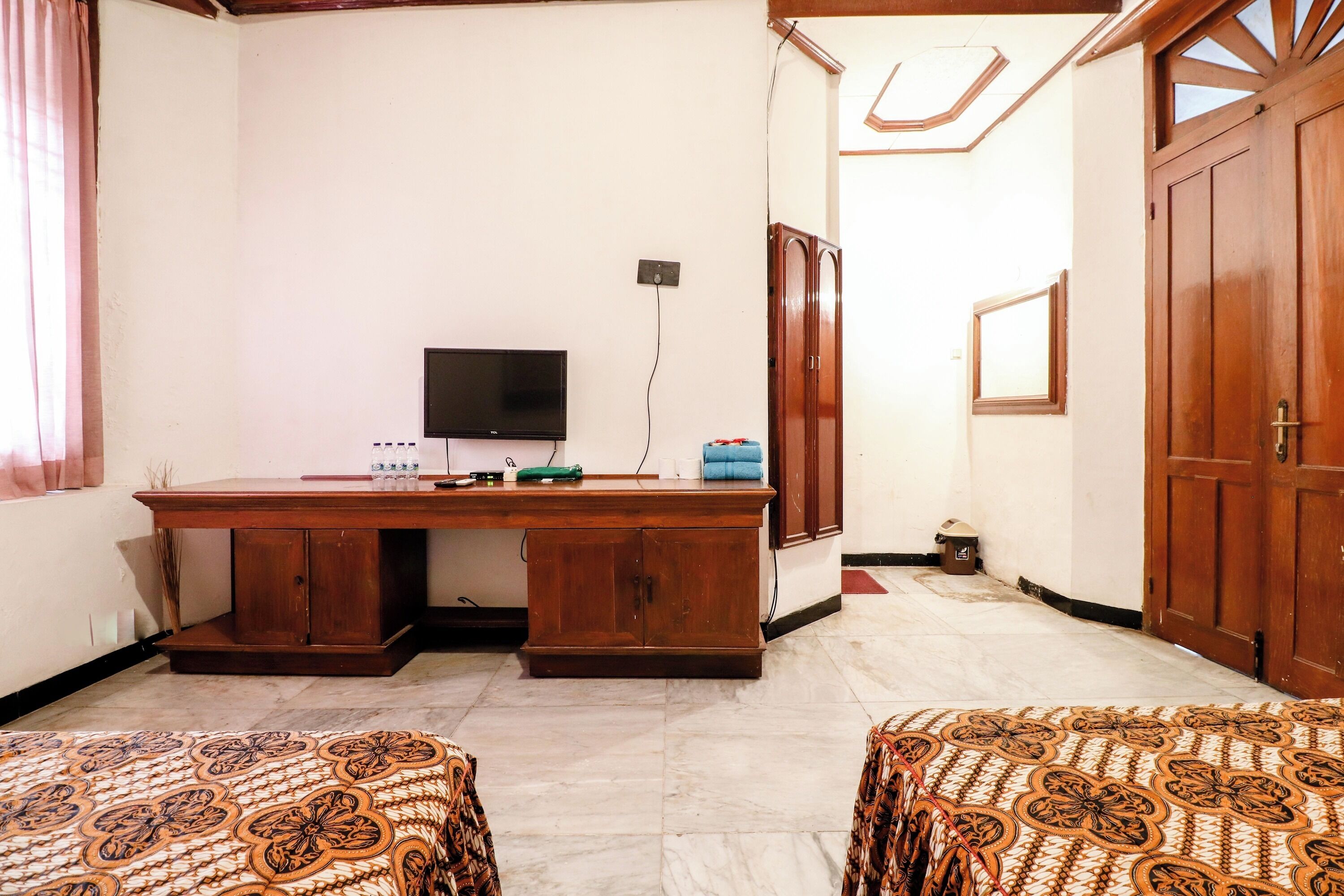 A room with a wooden desk, a television, and patterned bedspreads.