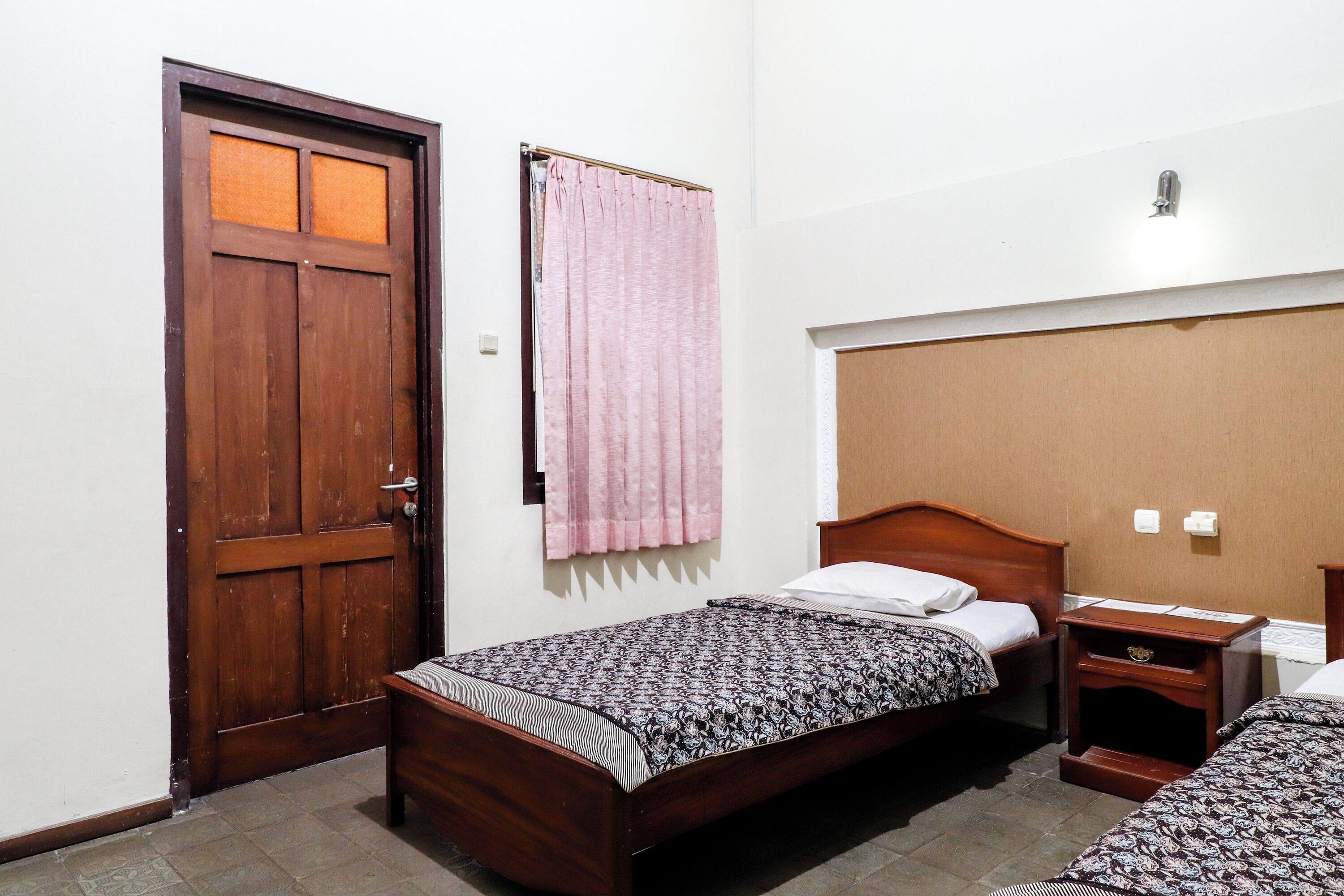 A room with two wooden beds, a wooden nightstand, a wooden door, and a pink curtain.