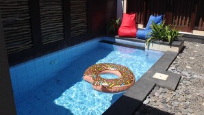 A swimming pool with a donut float, a stone wall, and a seating area with cushions. - Jukung Villas Kuta (Kuta)