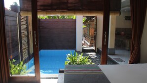 A room with a bed, a view of a swimming pool, and a small garden area with plants. - Jukung Villas Kuta (Kuta)