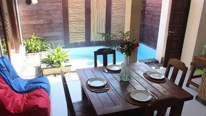 A wooden dining table set for four with plates, cutlery, and a vase with flowers. - Jukung Villas Kuta (Kuta)