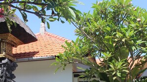 A traditional house with a tiled roof, a thatched roof structure, and a small garden with various plants and a stone pathway. - Jukung Villas Kuta (Kuta)