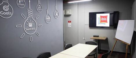 A conference room with a long table, chairs, a whiteboard, and a screen displaying the ibis logo.