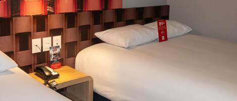 Une chambre d’hôtel avec deux lits, une table de chevet avec un téléphone, un panneau rouge et un mur orné d’un motif géométrique.