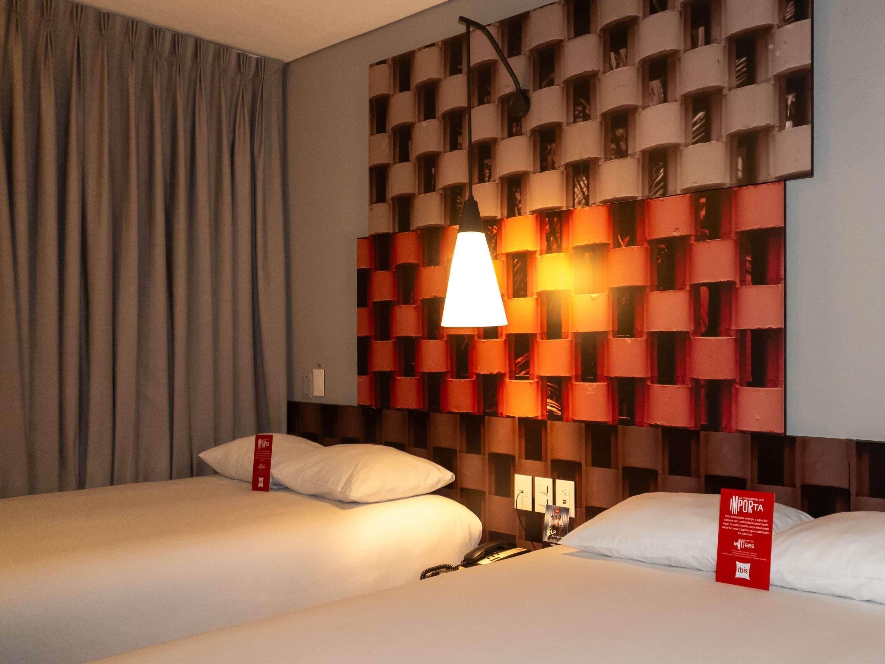 Una camera d'albergo con due letti, una lampada a muro e un cartello rosso.