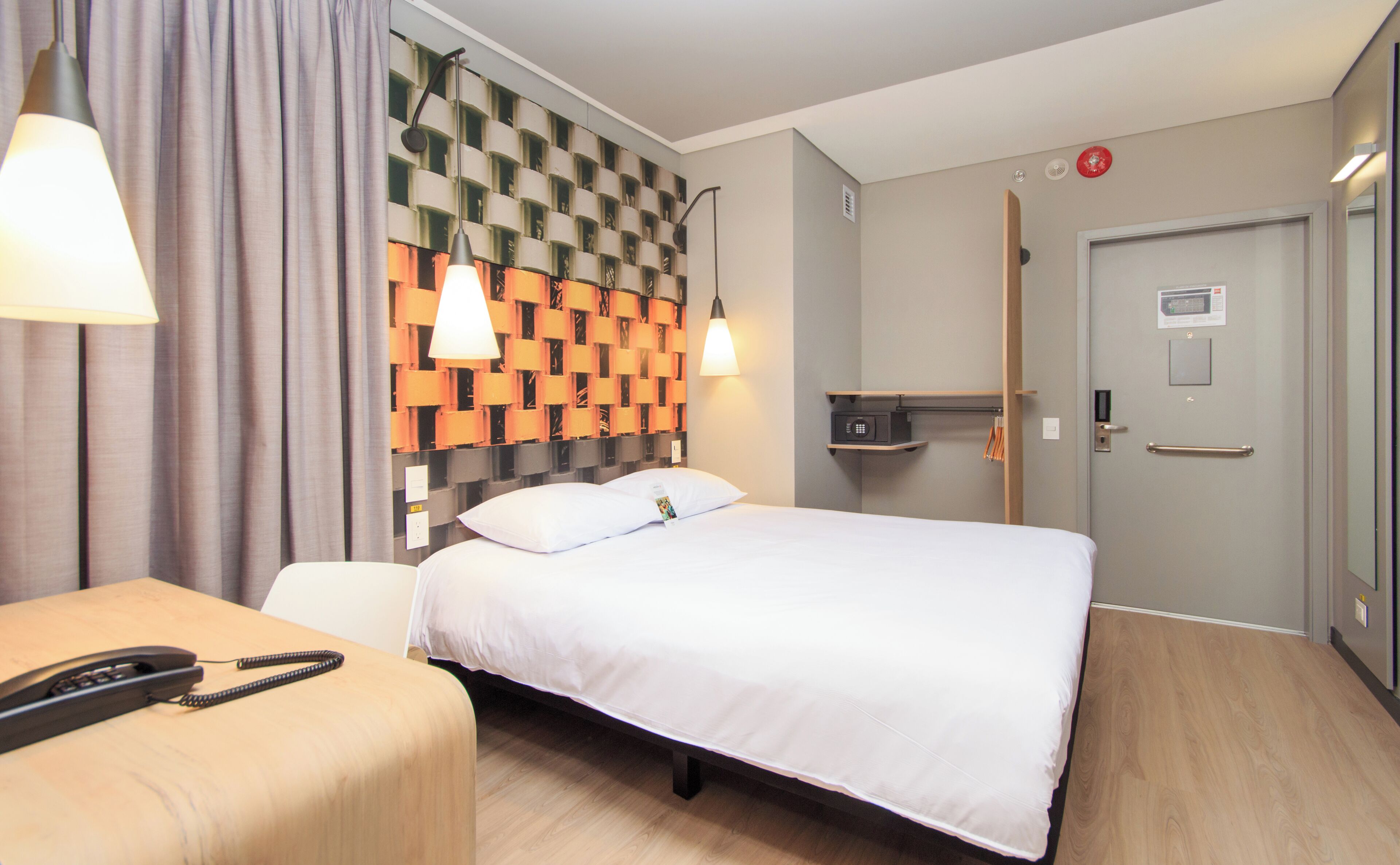 A hotel room with a bed, bedside table, lamp, and a wall with a patterned design.