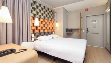 A hotel room with a bed, bedside table, lamp, and a wall with a patterned design.