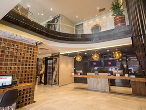 Un moderno vestíbulo de hotel con mostrador de recepción, zona de estar y una escalera que sube a un nivel superior.