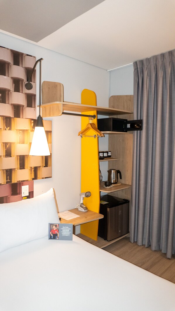 Una habitación de hotel compacta con una cama, una kitchenette pequeña, un zapatero colgante y un estante en la pared.