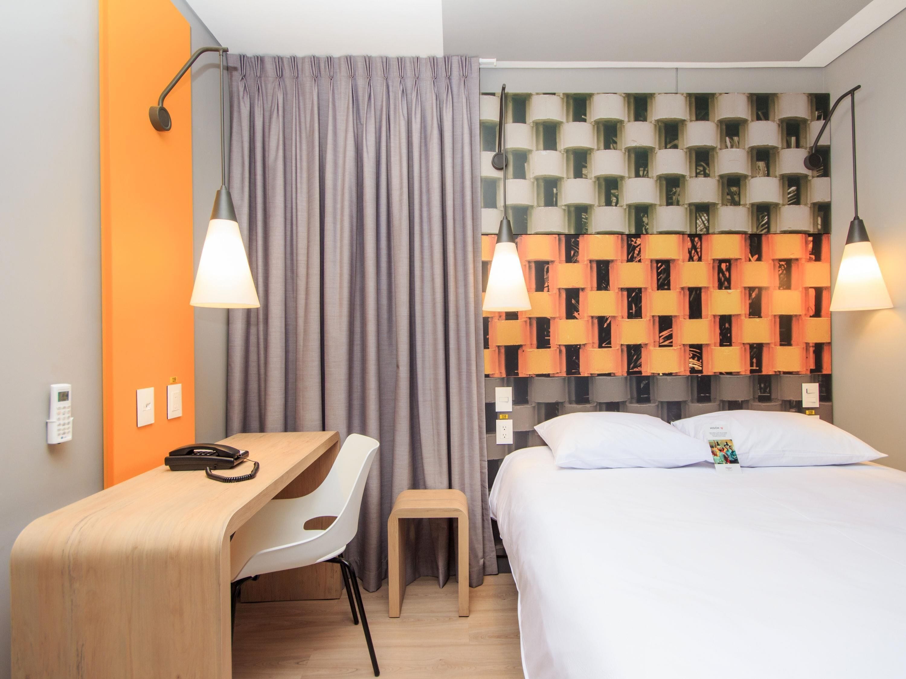 A hotel room with a desk, chair, bed, and a patterned headboard.