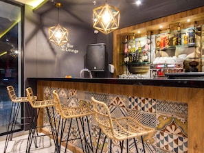 Espaço de bar/lounge com cadeiras de vime, balcão e variedade de garrafas de bebidas.
