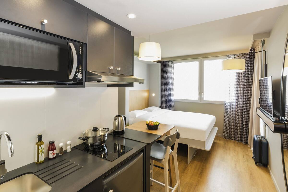 Une chambre d’hôtel compacte comprenant un coin cuisine, un lit, un bureau et un téléviseur.