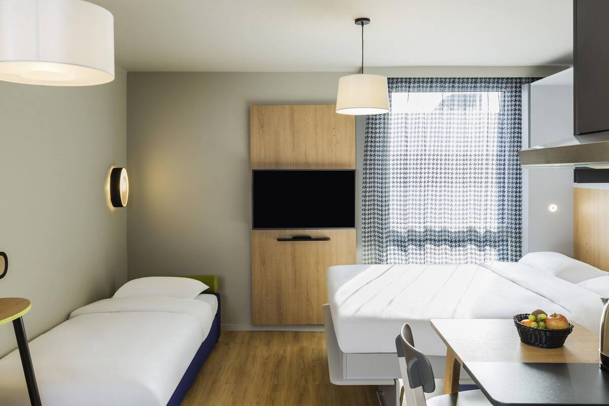 Une chambre d’hôtel moderne équipée d’un lit, d’un bureau avec une chaise, d’une télévision et d’une fenêtre agrémentée de rideaux à motifs.