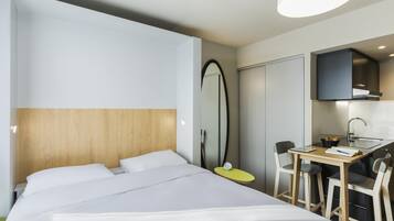 Une chambre d’hôtel comprenant un lit, un bureau avec une chaise, un miroir et une kitchenette.
