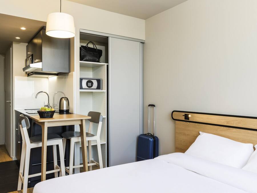 Quarto de hotel com cama, escrivaninha com cadeiras, mala, micro-ondas e guarda-roupa.