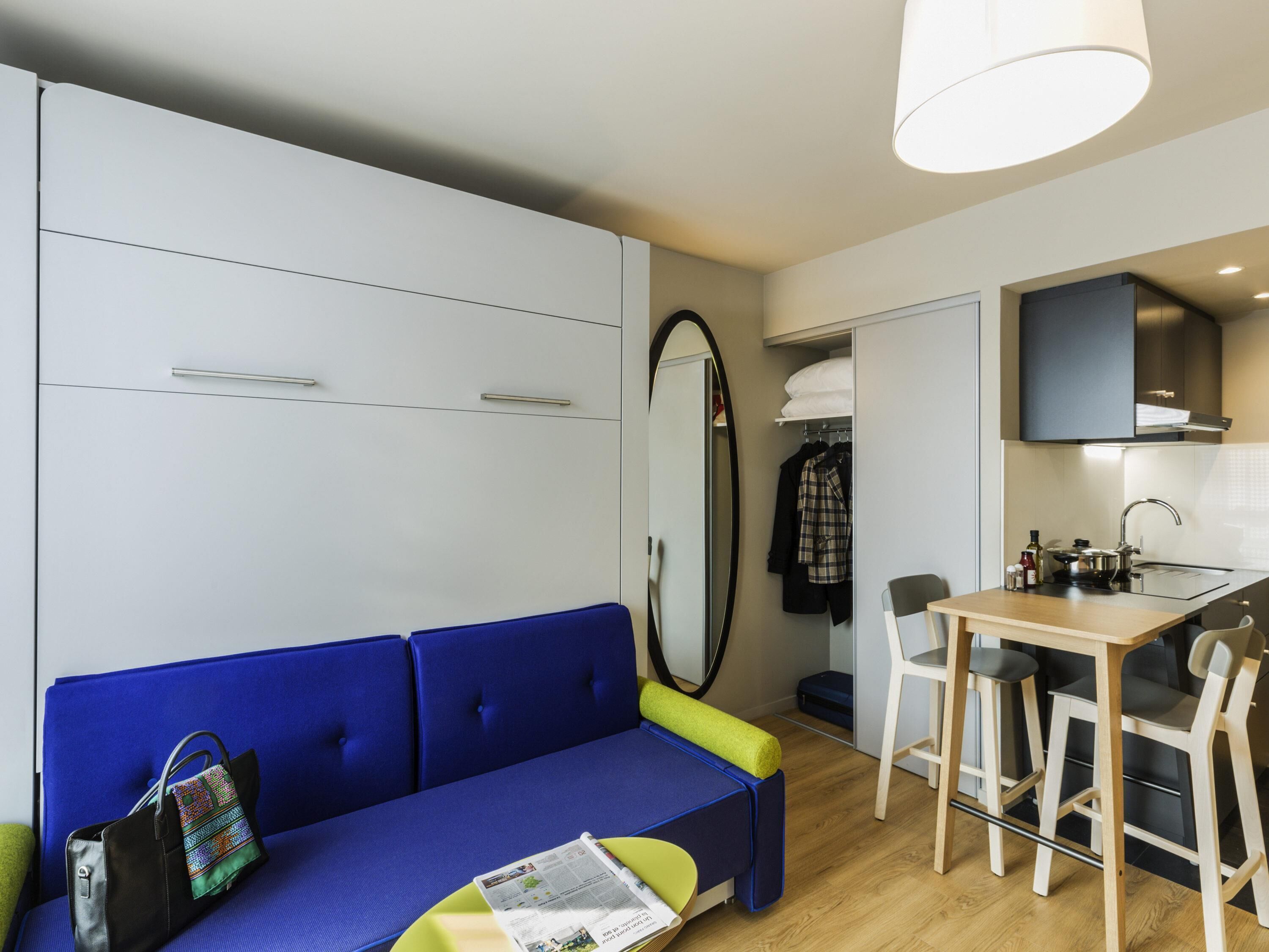 A compact living space with a sofa, a dining table with chairs, a kitchenette, and a wardrobe.