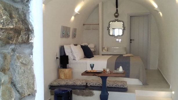 Una habitación acogedora y bien iluminada, con una pared de piedra, un banco curvo, una mesita y una escalera que sube a un nivel superior.