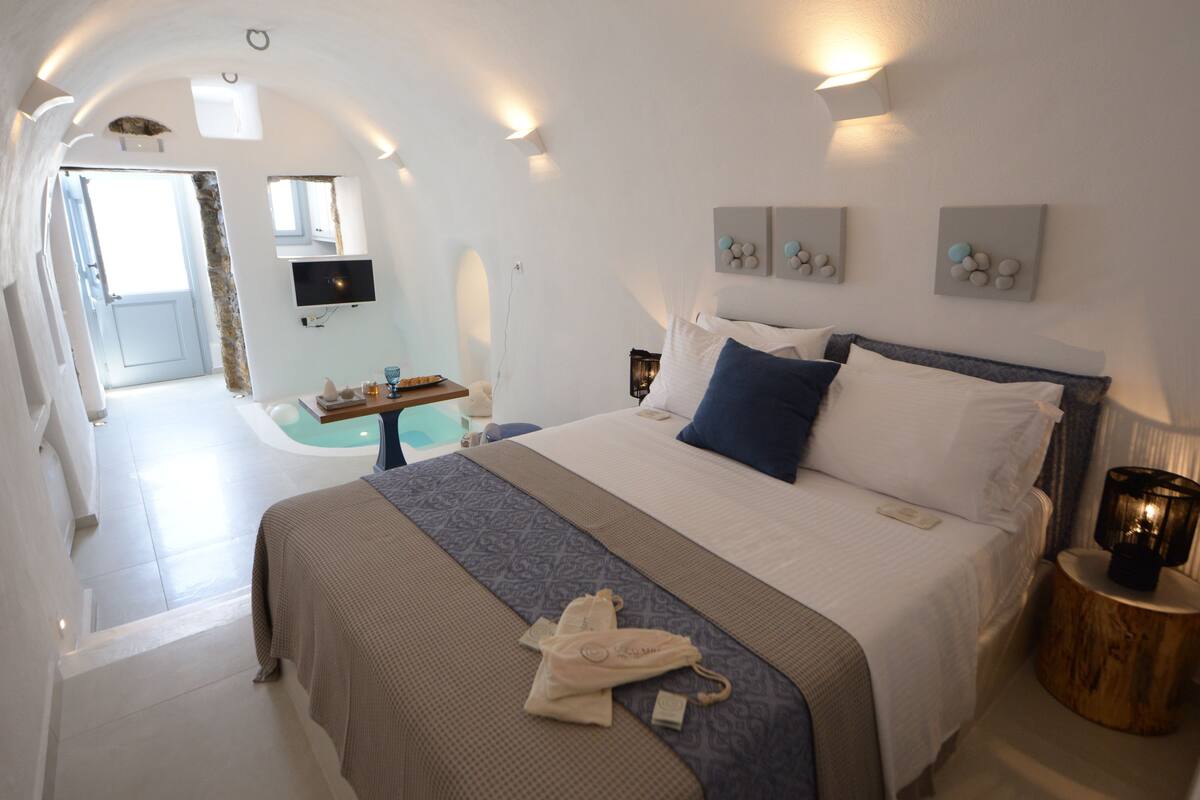 Une chambre d’hôtel moderne dotée d’un grand lit, d’une table de chevet, d’un téléviseur à écran plat et d’une salle de bain visible à travers une porte ouverte.