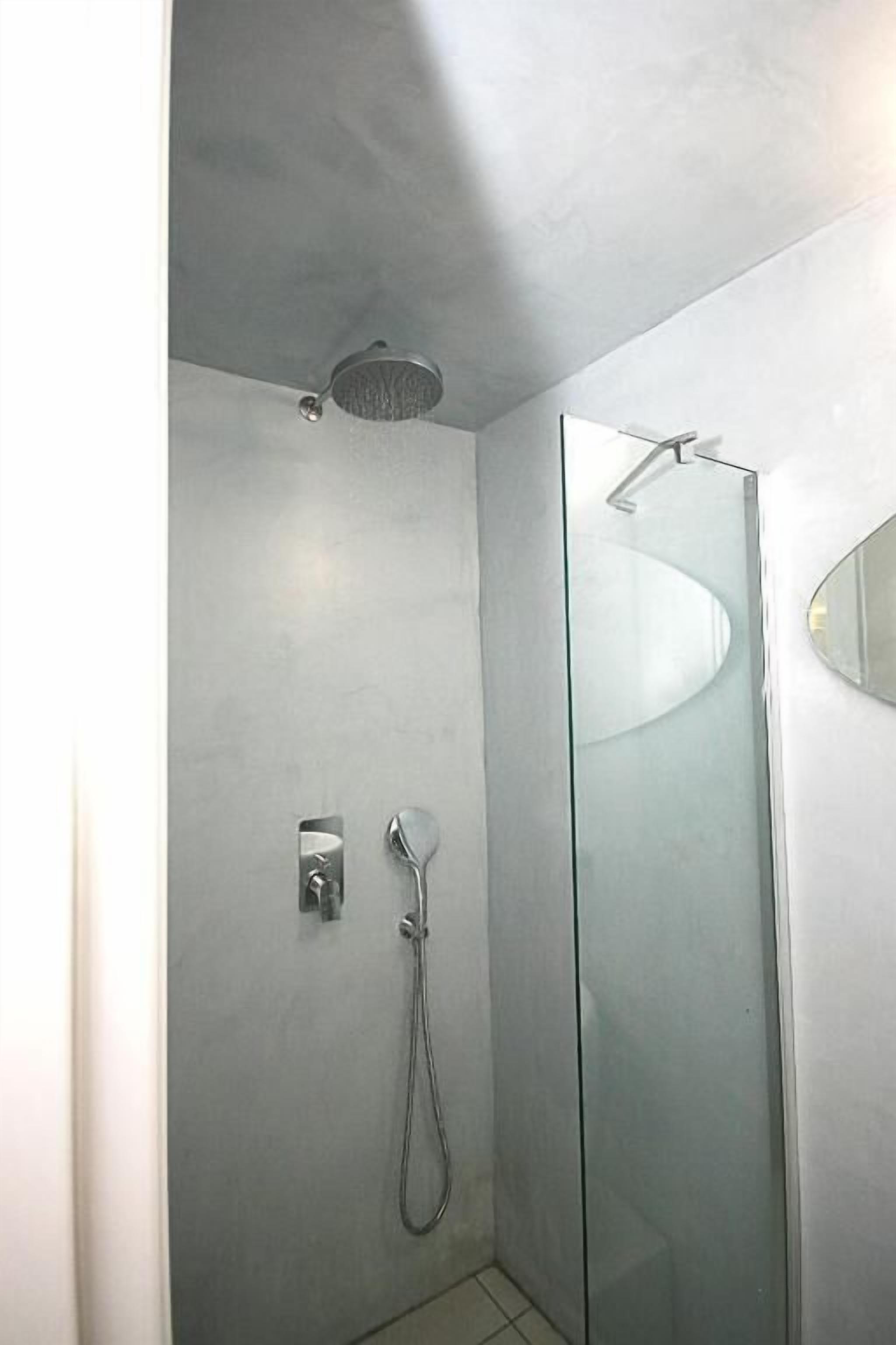 Um chuveiro moderno com divisória de vidro, chuveiro manual e painel de controle fixado na parede.