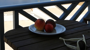 Una mesa con un plato de fruta y gafas de sol, con vistas a un paisaje costero con edificios y colinas.