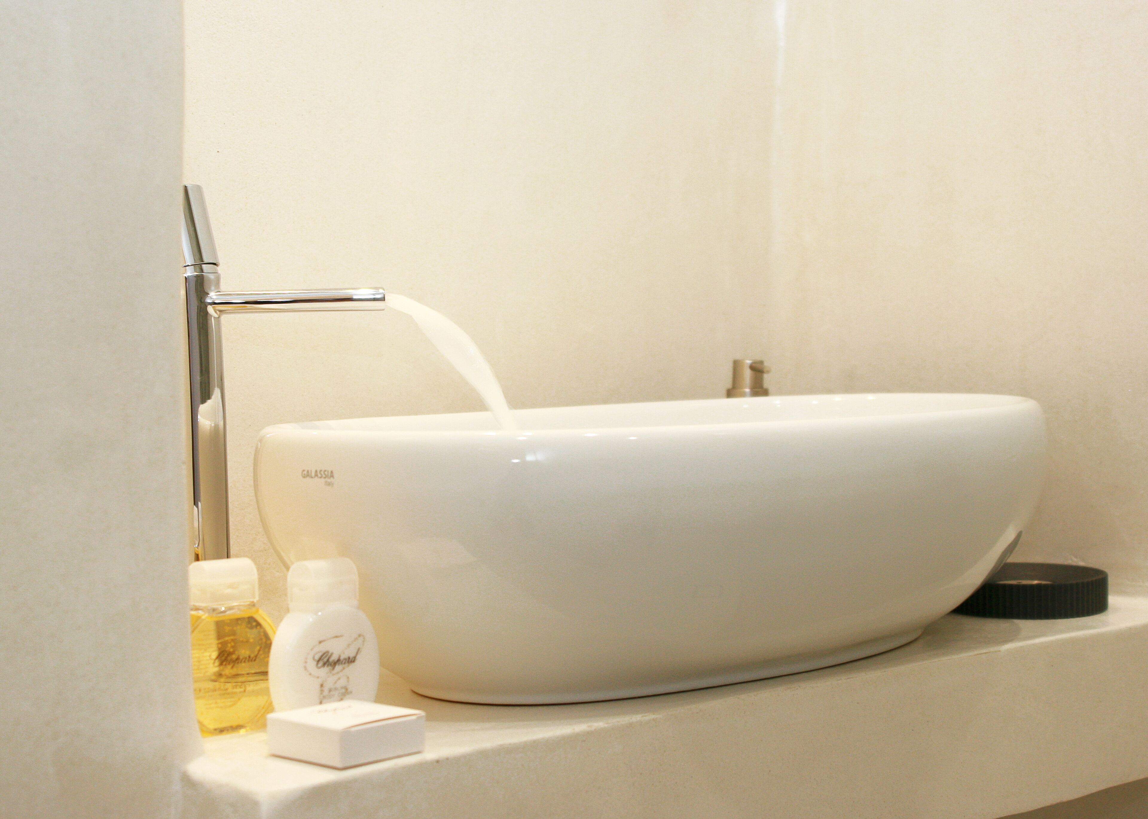 A white Galassia sink with a chrome faucet, two bottles of perfume, and a black soap dish on a countertop.