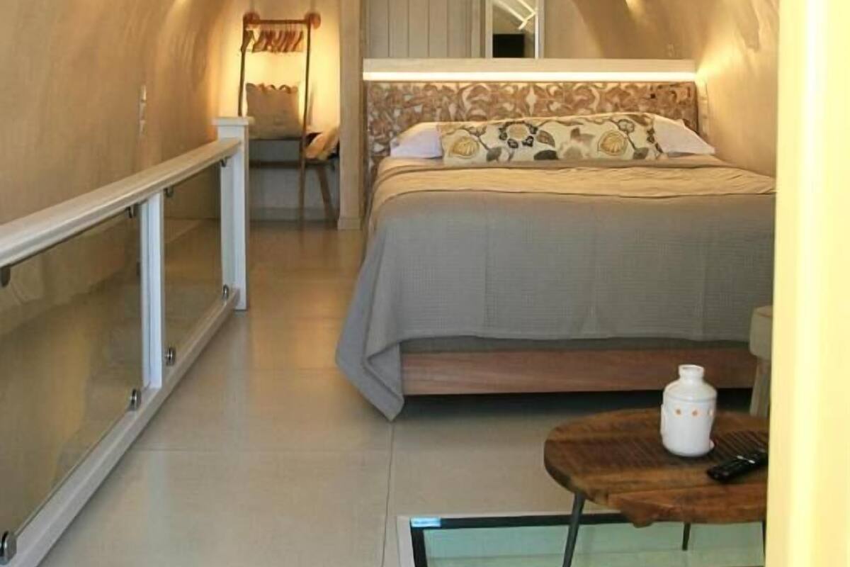 Une chambre à coucher de taille réduite, dotée d’une forme en arc, comprenant un lit, une table de chevet et une cloison en verre.