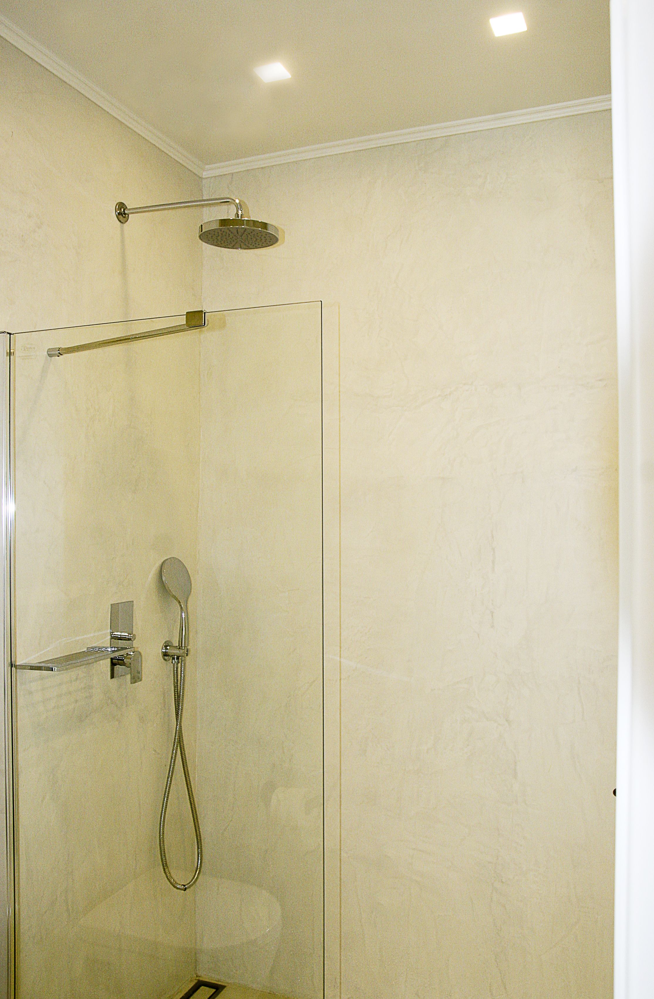 A glass-enclosed shower with a handheld showerhead and a wall-mounted faucet.