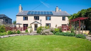 A two-story house with a solar panel roof, a front porch, and a red pergola. - Cadleigh Manor B&B (Ivybridge)