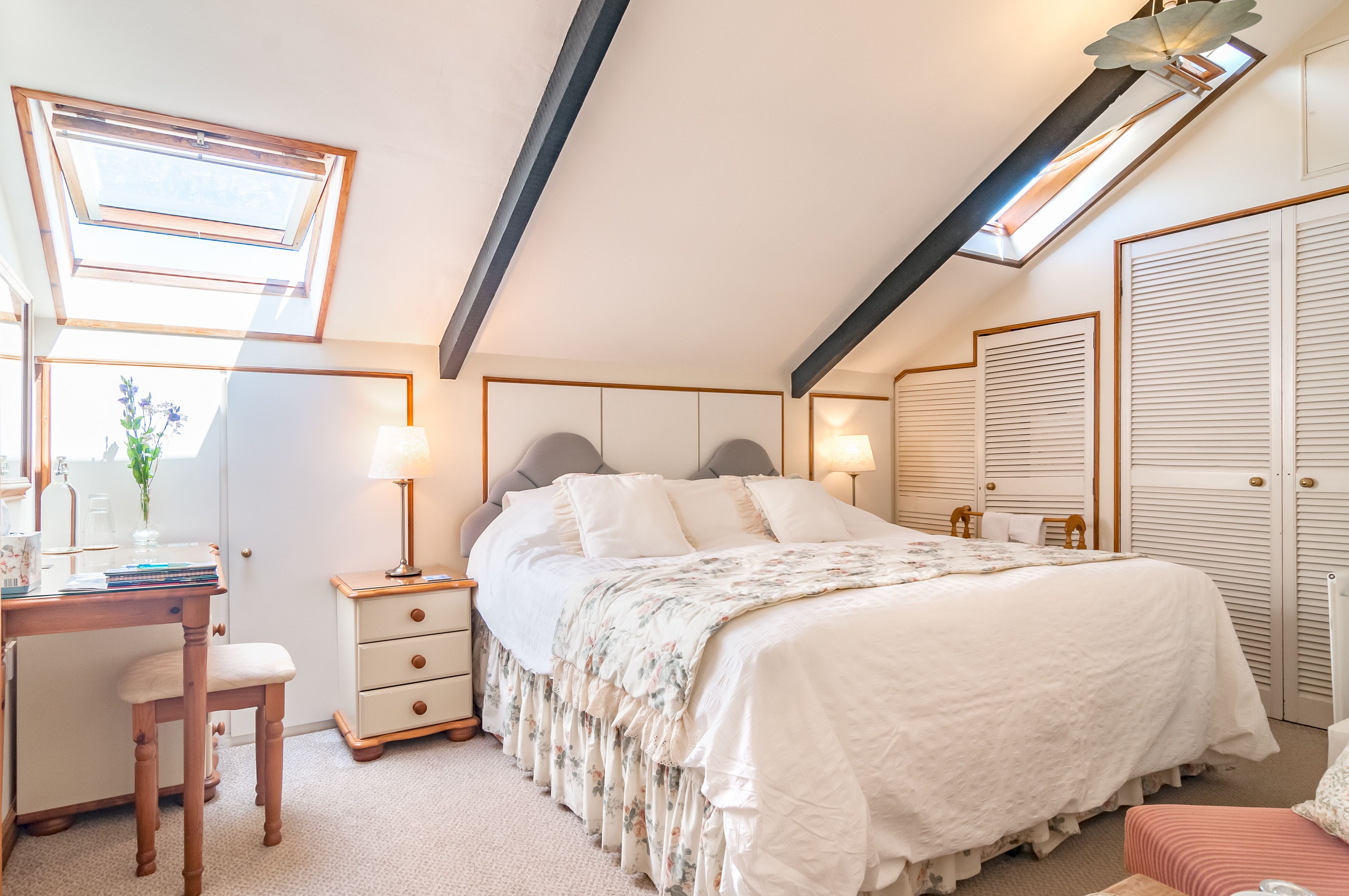 Een slaapkamer met dakraam, een bed met bloemenprint, een bureau met stoel en een kledingkast.