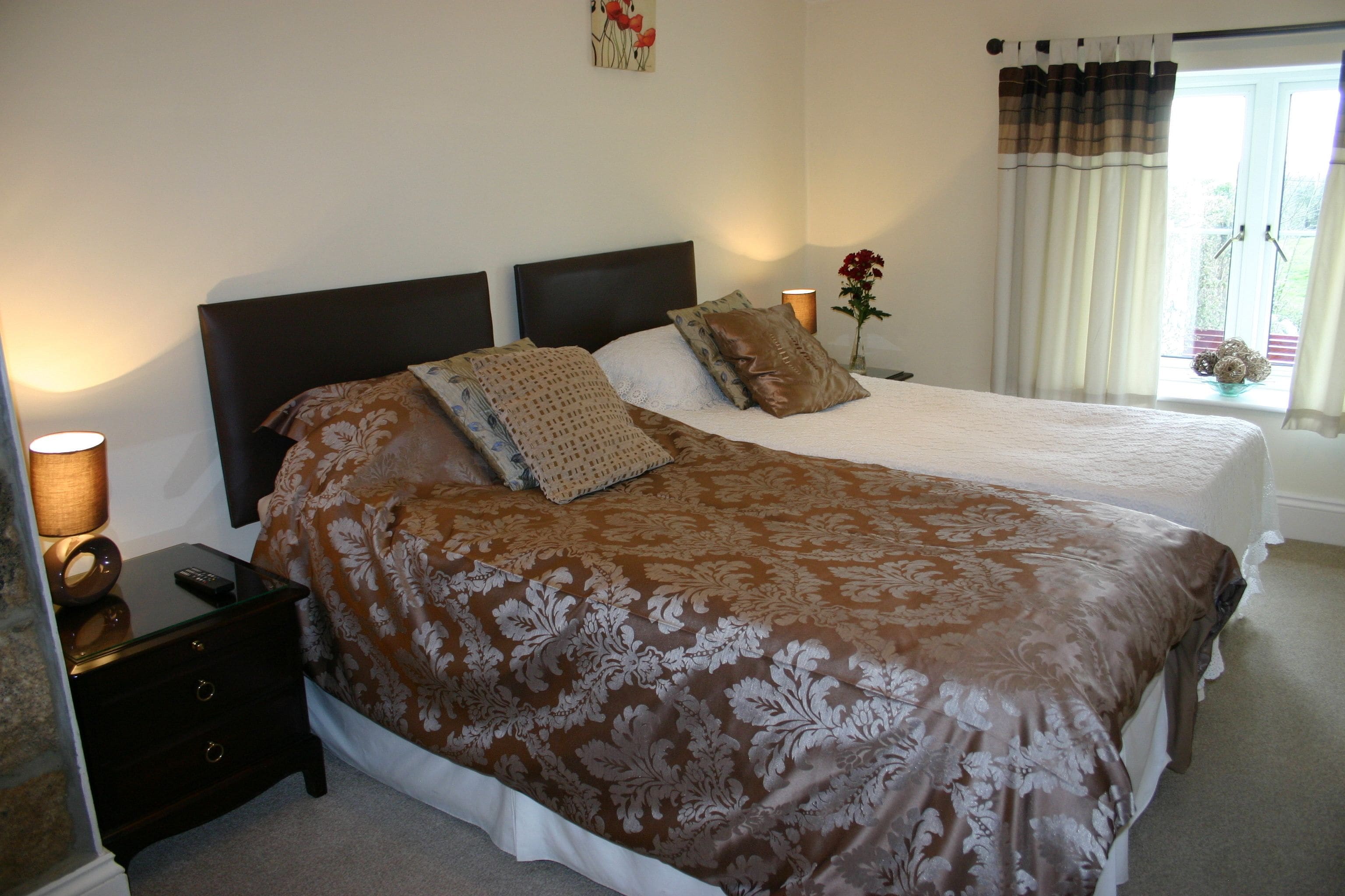 A double bed with a brown floral bedspread, a nightstand with a lamp, and a window with curtains.