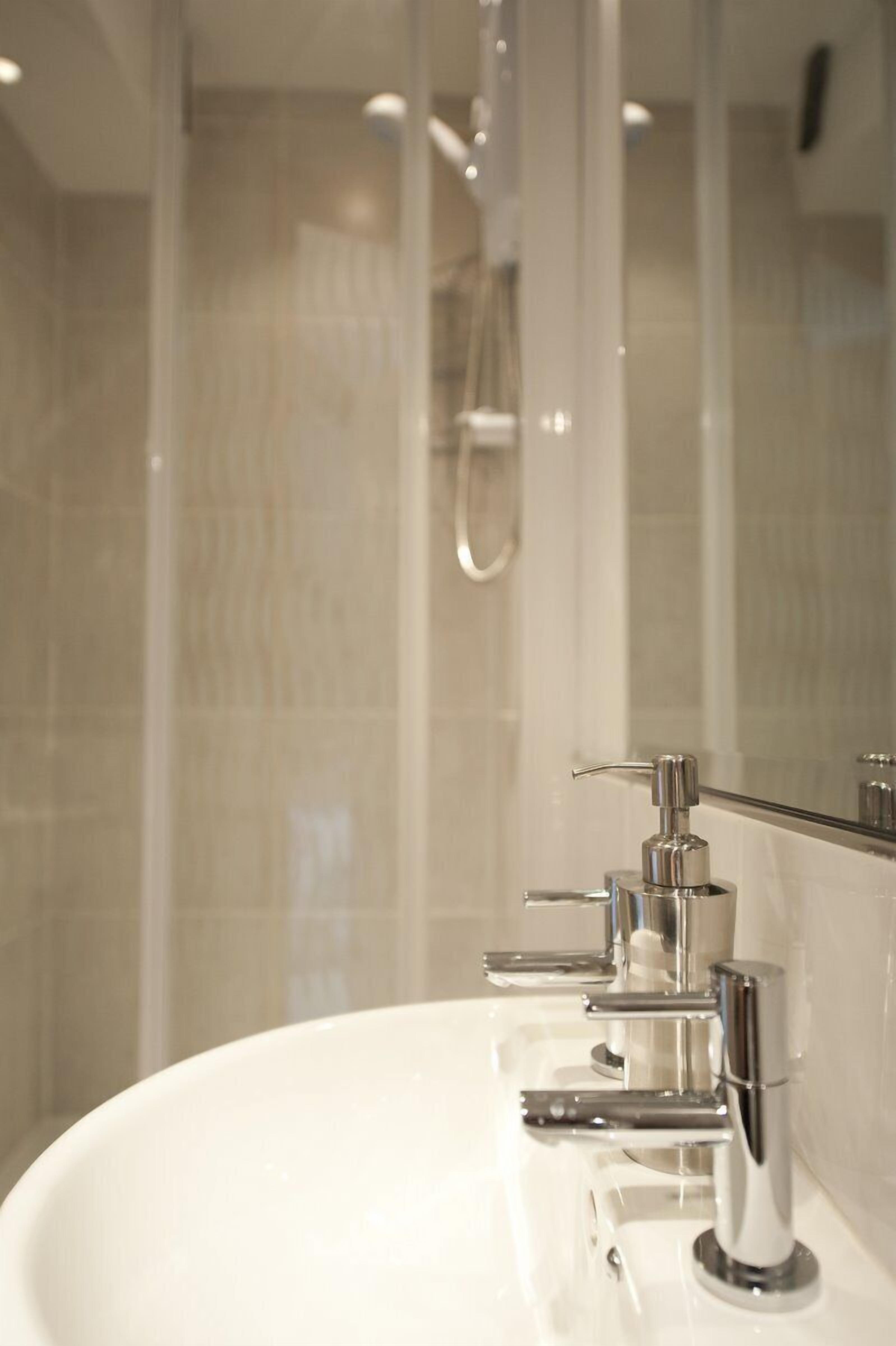 Un bagno moderno con un lavabo bianco, rubinetti cromati e cabina doccia in vetro.