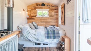 A cozy bedroom with a bed, a window, a wooden wall, and a small shelf. - Cadleigh Manor B&B (Ivybridge)