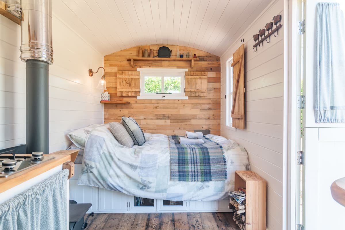 Une chambre confortable avec un lit, une fenêtre, un mur en bois et une petite étagère.