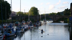 A marina with boats docked, a person kayaking, and a stone bridge in the background. - Cadleigh Manor B&B (Ivybridge)