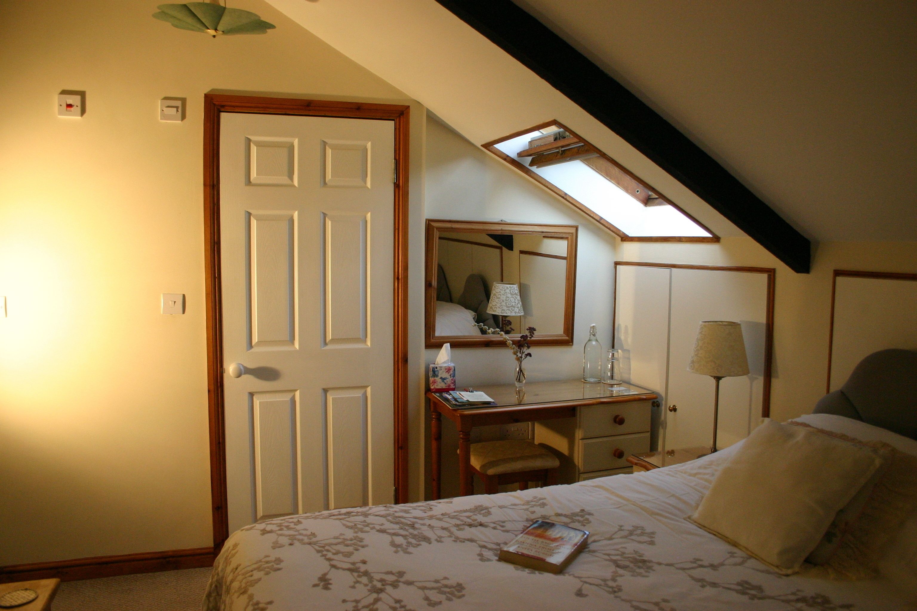 A bedroom with a bed, a desk, a chair, a mirror, and a skylight.