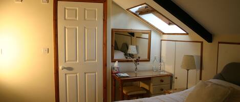 A bedroom with a bed, a desk, a chair, a mirror, and a skylight.