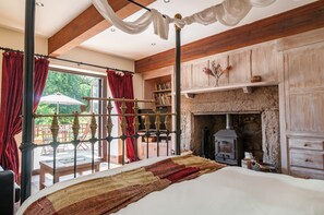 A bedroom with a large bed, a stone fireplace, wooden beams, and a view of the outdoors. - Cadleigh Manor B&B (Ivybridge)